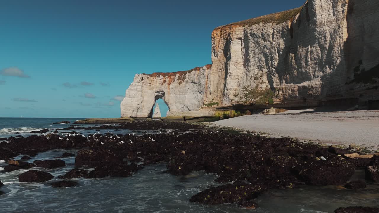 Wide view of Étretat’s chalk cliffs and natural arch with waves and seabirds flying away