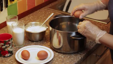 rompiendo huevos en una cacerola grande con ingredientes para harina y vasos de leche