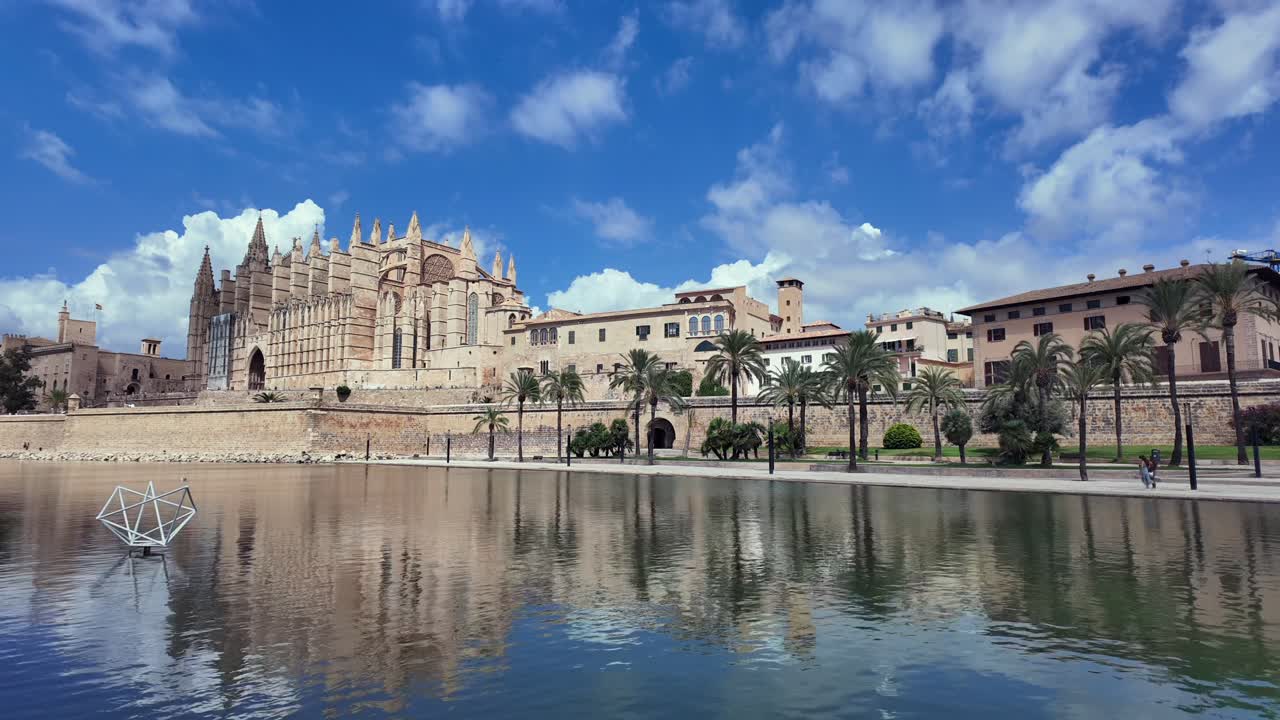 A timelapse of Palma de Mallorca historical city center and its cathedral reflected on the water under a blue sky with changing storm clouds