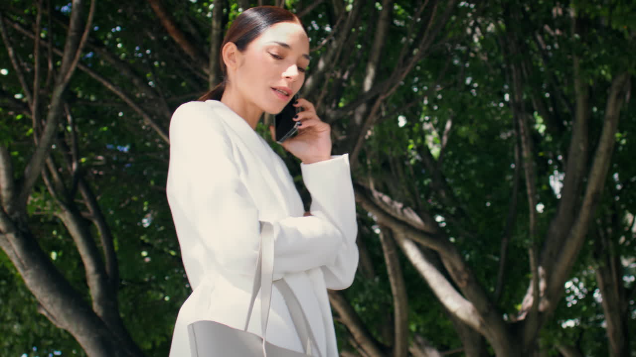 성공한 사업가 여성이 전화를 걸고 나무에 서 있습니다. 소녀가 전화를 하고 있습니다.