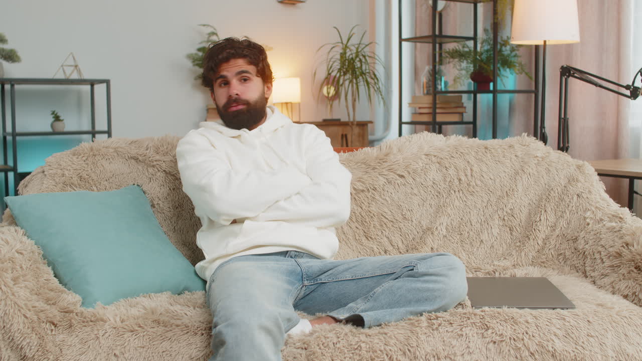 Tired exhausted young indian man freelancer sitting on couch closing laptop in living room at home