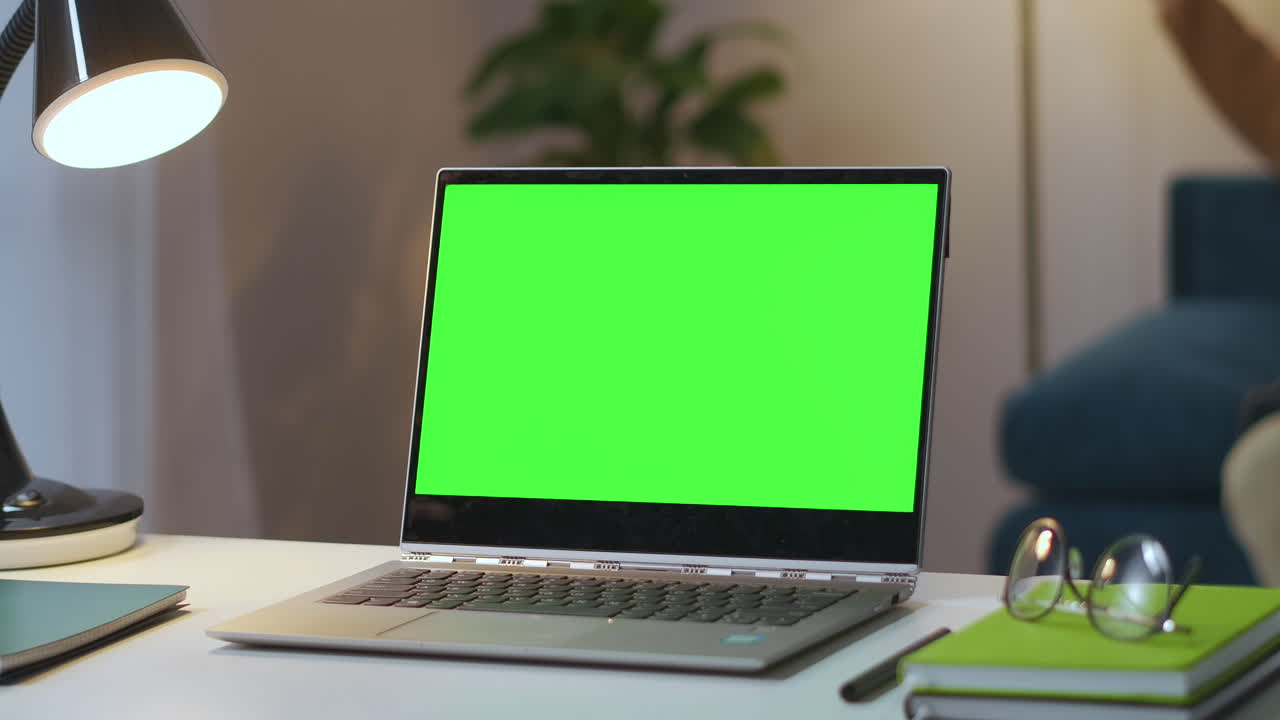 laptop aperto con schermo verde sul tavolo di lavoro nel soggiorno uomo sta spegnendo la lampada sullo sfondo zoom shot che si avvicina al display chiave croma