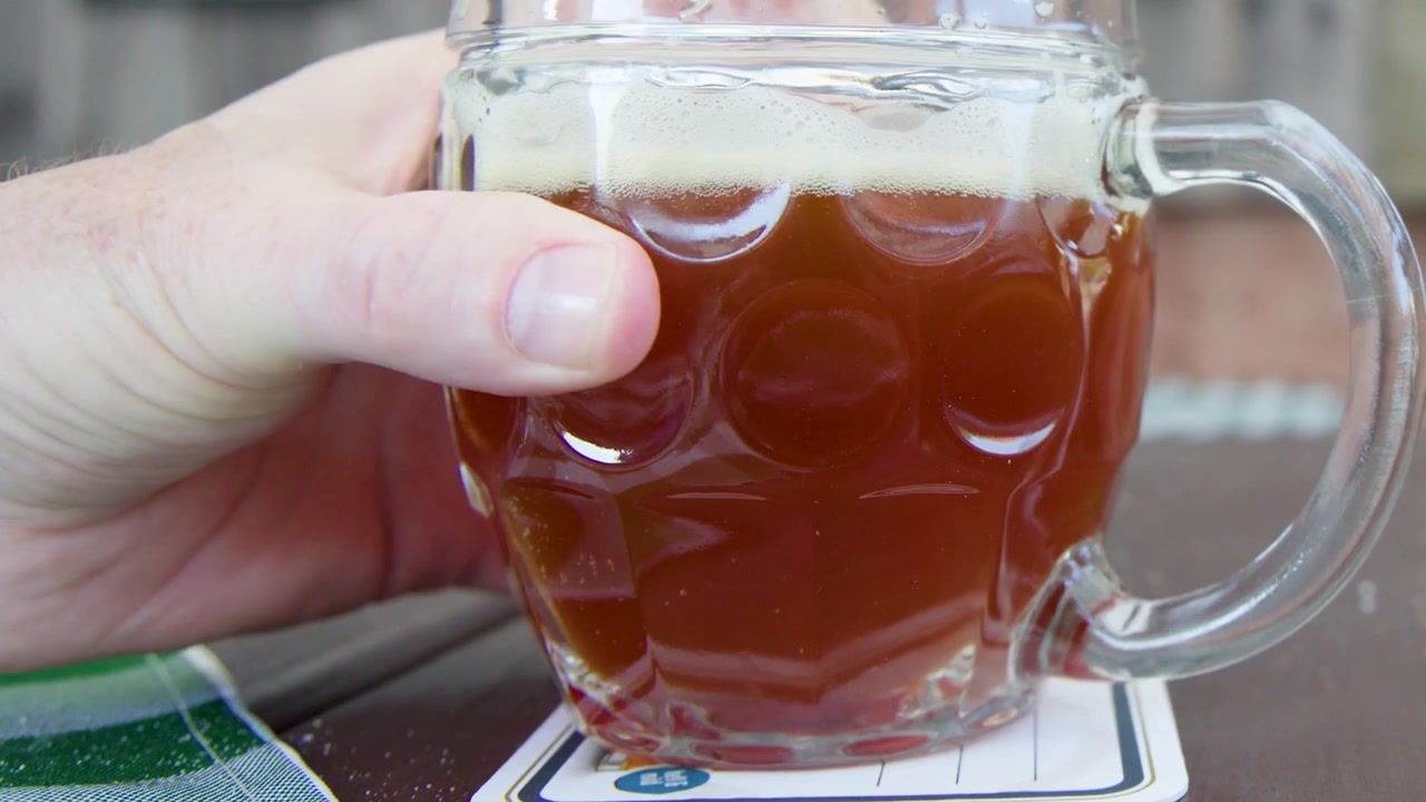 Una mano solleva e appoggia un tradizionale boccale da birra con fossette su un tavolo di legno.