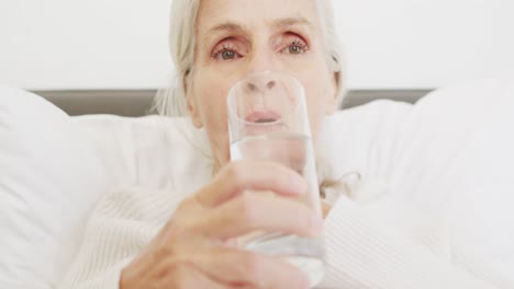 Video-Einer-Kaukasischen-Seniorin,-Die-Im-Bett-Wasser-Trinkt