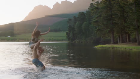 glückliches paar, das bei sonnenuntergang im see spritzt, junger mann holt seine freundin ab, spritzt im wasser, macht spaß, spielt, genießt romantische sommerliebe