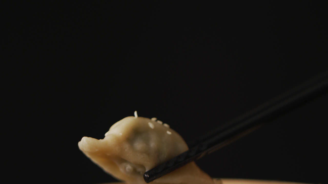 Chopsticks with gyoza dumpling in bamboo steamer on black background