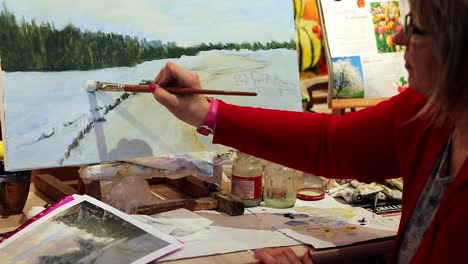 an elder woman is painting a winter oil art with a brush and oil paints