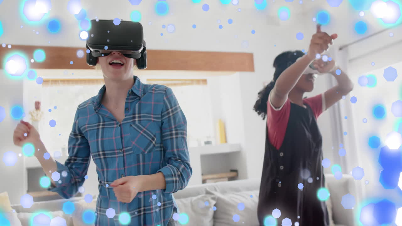 Animation of blue and white spots over two happy diverse teenage girls in dancing in vr headsets
