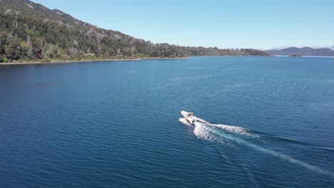 tracking aerial follows bright white motorboat speeding on blue lake