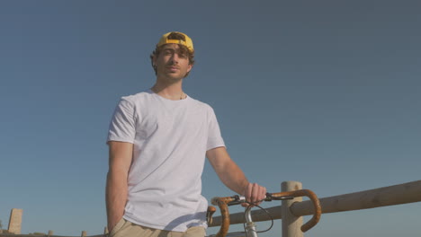 Man-With-Bike-Walking-Down-The-Boardwalk-Looking-At-The-Camera