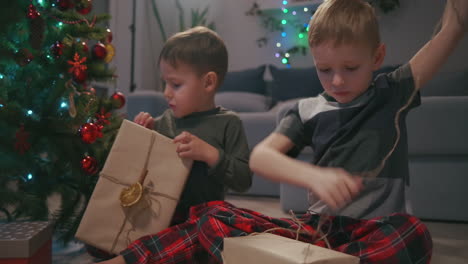 two boys unpack christmas presents under a christmas tree. children open gifts. high quality 4k footage