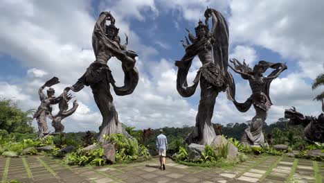 Ruhe-Entdecken:-Junger-Tourist-Nähert-Sich-Engelhaften-Steinstatuen-Im-Restaurant-Taman-Dedari,-Ubud,-Bali-–-4K-Push-in-Gimbal-Aufnahme