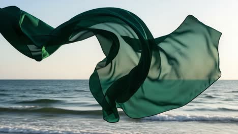 a graceful green fabric billows majestically in the ocean breeze, capturing the essence of fluidity and beauty against the serene backdrop of the calm sea and sky
