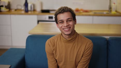 Portrait-young-curly-man-smiling-sitting-on-the-sofa-in-home-living-room