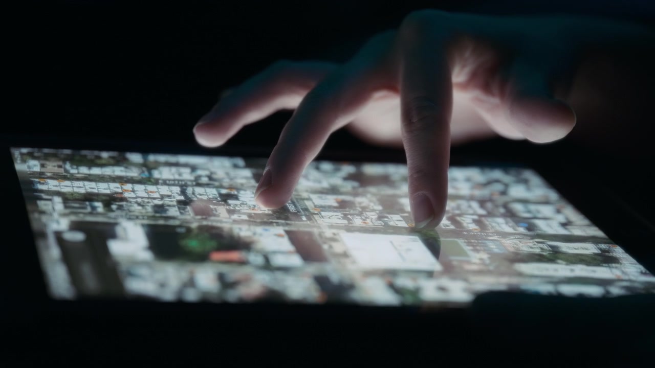 Person udforsker satellitvisning af et bykort på en tablet.