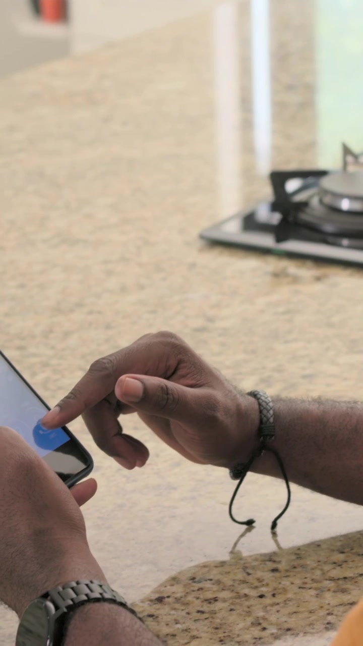 Vertical video: Tapping man in orange tee moving phone, tapping after blue dot appearing in kitchen