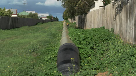 Incline-Hacia-Arriba-Una-Gran-Tubería-De-Agua-Por-Una-Avenida-Cubierta-De-Hierba-En-Un-Suburbio