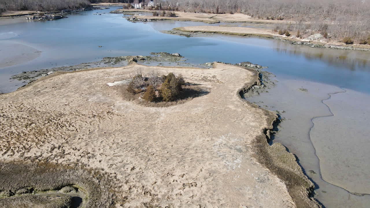 Slow aerial flight over mudflats, showing brackish water and the salt marshes