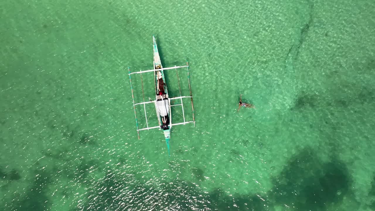Aerial View of a Person Swimming Near a Banca Boat in Clear Turquoise Water