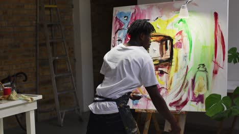 Rear-view-of-african-american-male-artist-wearing-apron-painting-on-canvas-at-art-studio