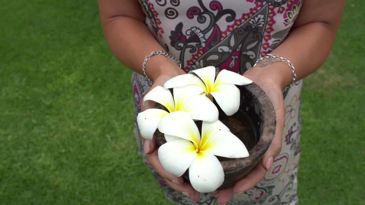 vista panorámica de una mujer que está de pie sobre la hierba y muestra plumeria hawaiana blanca con las manos