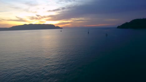 Die-Untergehende-Sonne-Versinkt-Hinter-Kleinen-Bergen-An-Der-Küste-Von-Costa-Rica,-Während-Boote-Im-Ruhigen-Wasser-Der-Ballena-Bay-Vor-Anker-Liegen