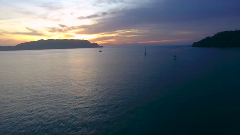 el sol se pone debajo de pequeñas montañas en la costa de costa rica mientras los barcos están anclados en las tranquilas aguas de la bahía de ballena