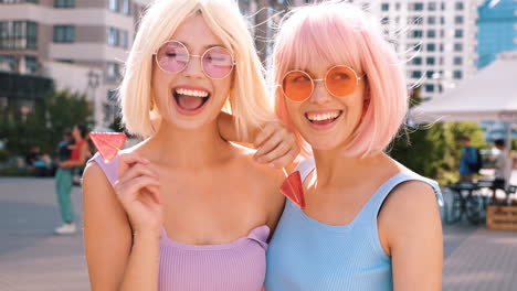 two happy women with pink and blonde wigs enjoying lollipops on the city street