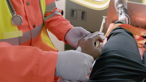 paramedic wearing facial mask touching the hand of a patient lying on the stretcher inside an ambulance 1