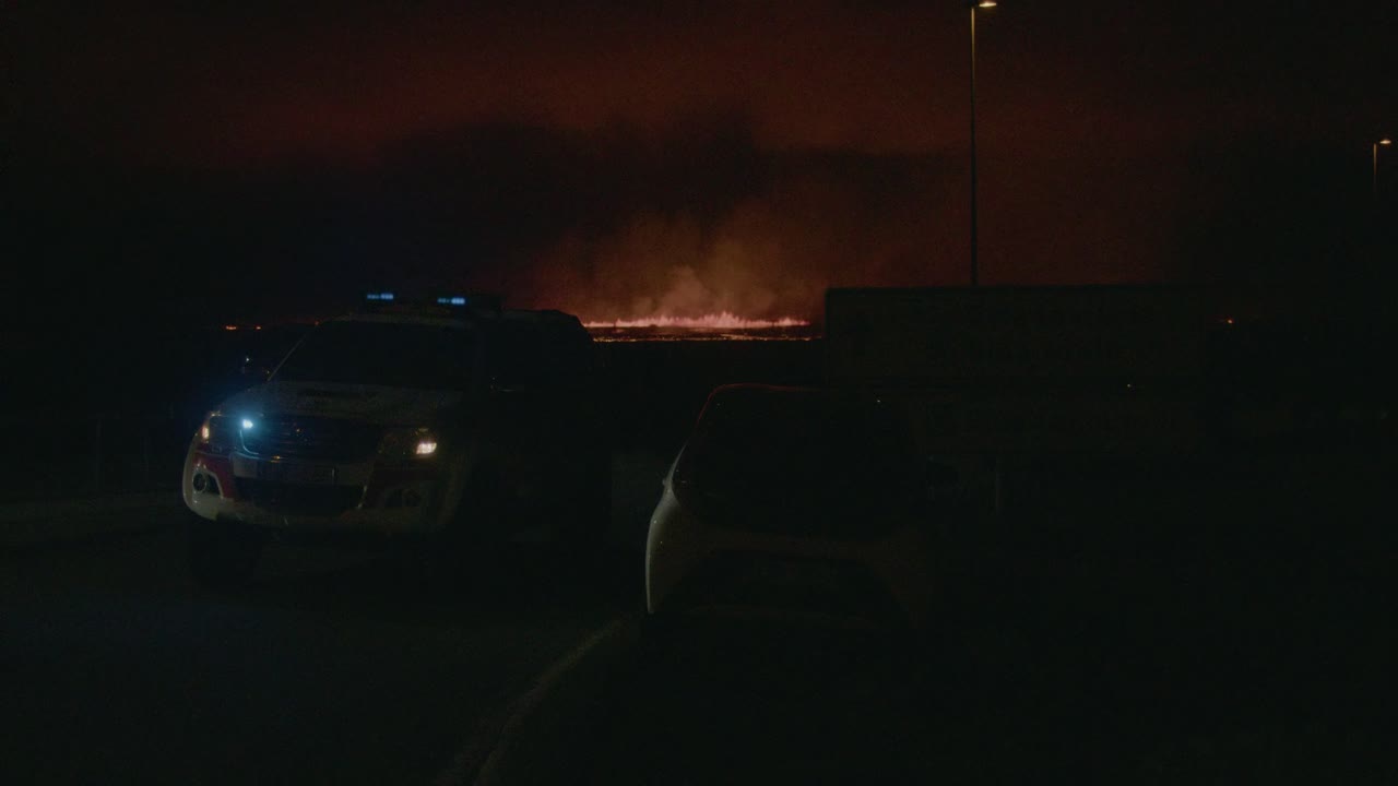 A police car blocks a road as fire and lava from the Grindavik volcano in Sundhnúkur crater, Iceland, erupt in the distance.