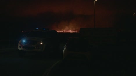 a police car blocks a road as fire and lava from the grindavik volcano in sundhnúkur crater, iceland, erupt in the distance.