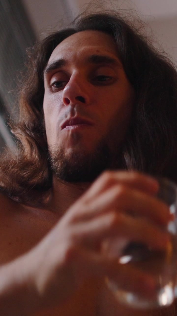 Giovane uomo con capelli lunghi che beve acqua da un bicchiere