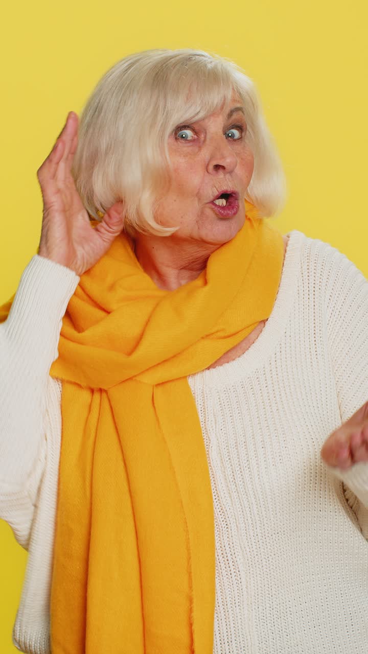 Anziana signora che cerca di sentirti, con espressione confusa e accigliata, che tiene un braccio vicino all'orecchio per sentire la voce più forte