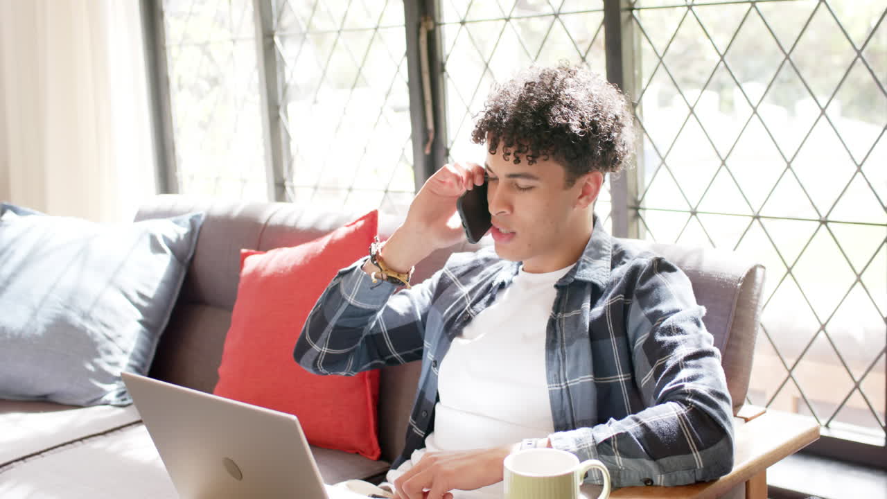 노트북을 사용하고 스마트폰으로 대화하는, 느린 동작을 하는 집에서 일하는 두 인종의 남자