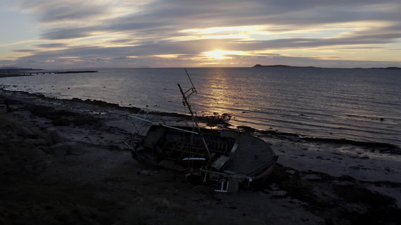 AERIAL - Shipwreck, boat on a beach at sunset in Kintyre, Scotland, wide static shot