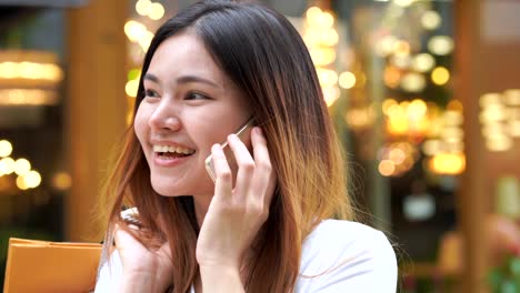 beautiful girl is calling to someone and she wears sunglasses at white shirt, she is happily shopping at the street mall, she holds several bags of paper and mobile.