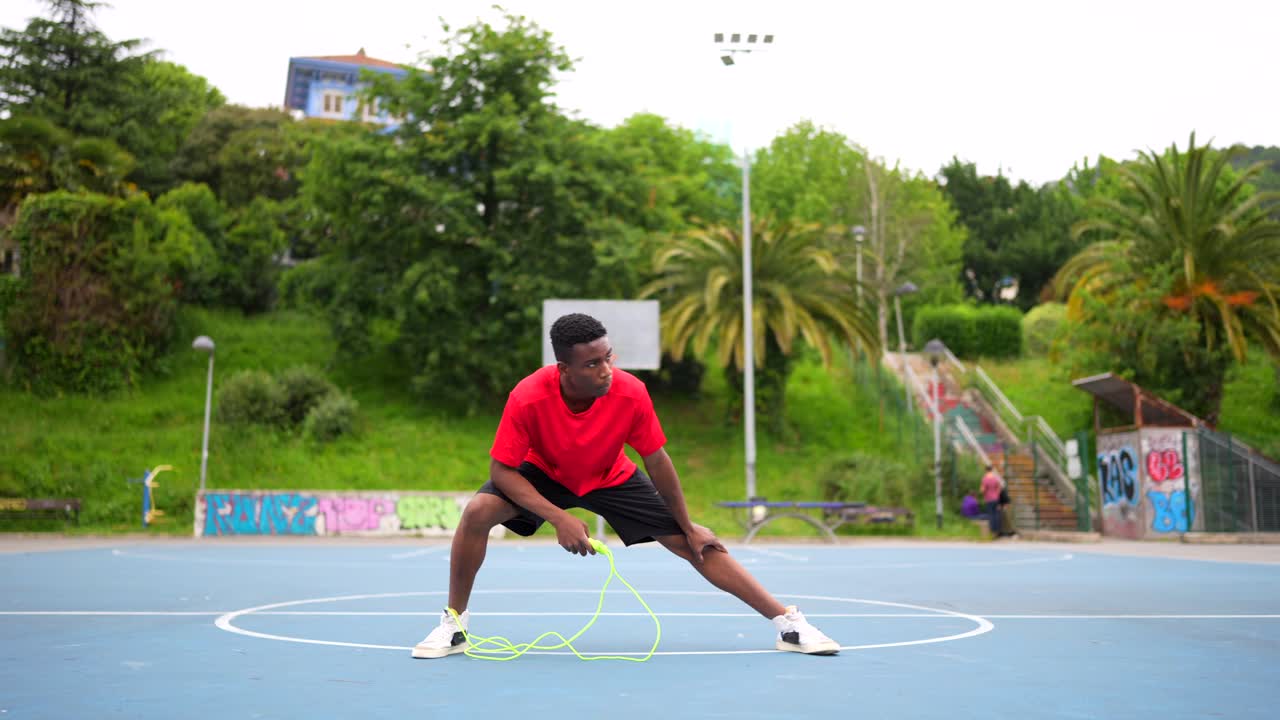 A man warms up and stretches with a jump rope on an outdoor basketball court