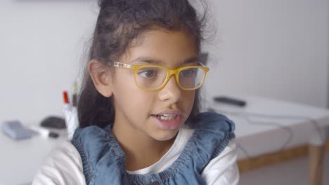 alumna latina inteligente y alegre con gafas sentada en un escritorio