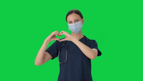 doctora india feliz mostrando el signo del corazón con la pantalla verde de la máscara