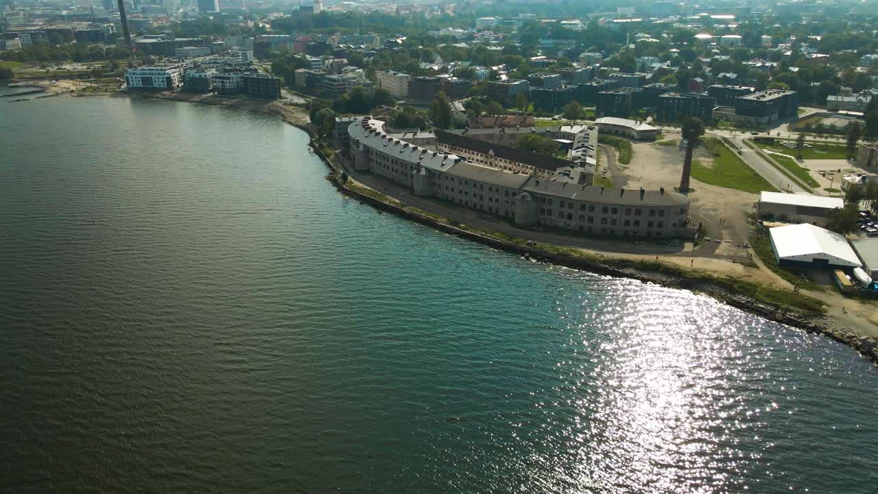 Vista aerea di un grande e antico complesso carcerario d'epoca Patarei su una costa baltica con oceano blu e verde durante una giornata estiva soleggiata. Sullo sfondo sono visibili moderni edifici residenziali