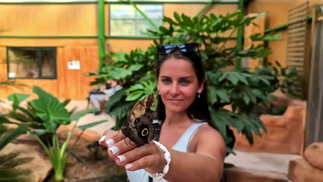 mujer sosteniendo una mariposa en la mano en un jardín botánico
