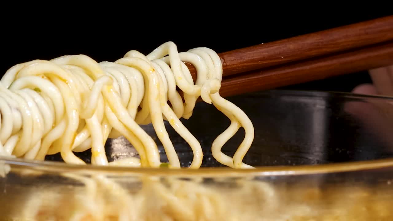 透明なガラスの丼の上で黄色いラーメンをねじり上げる木製の箸の超クローズアップ