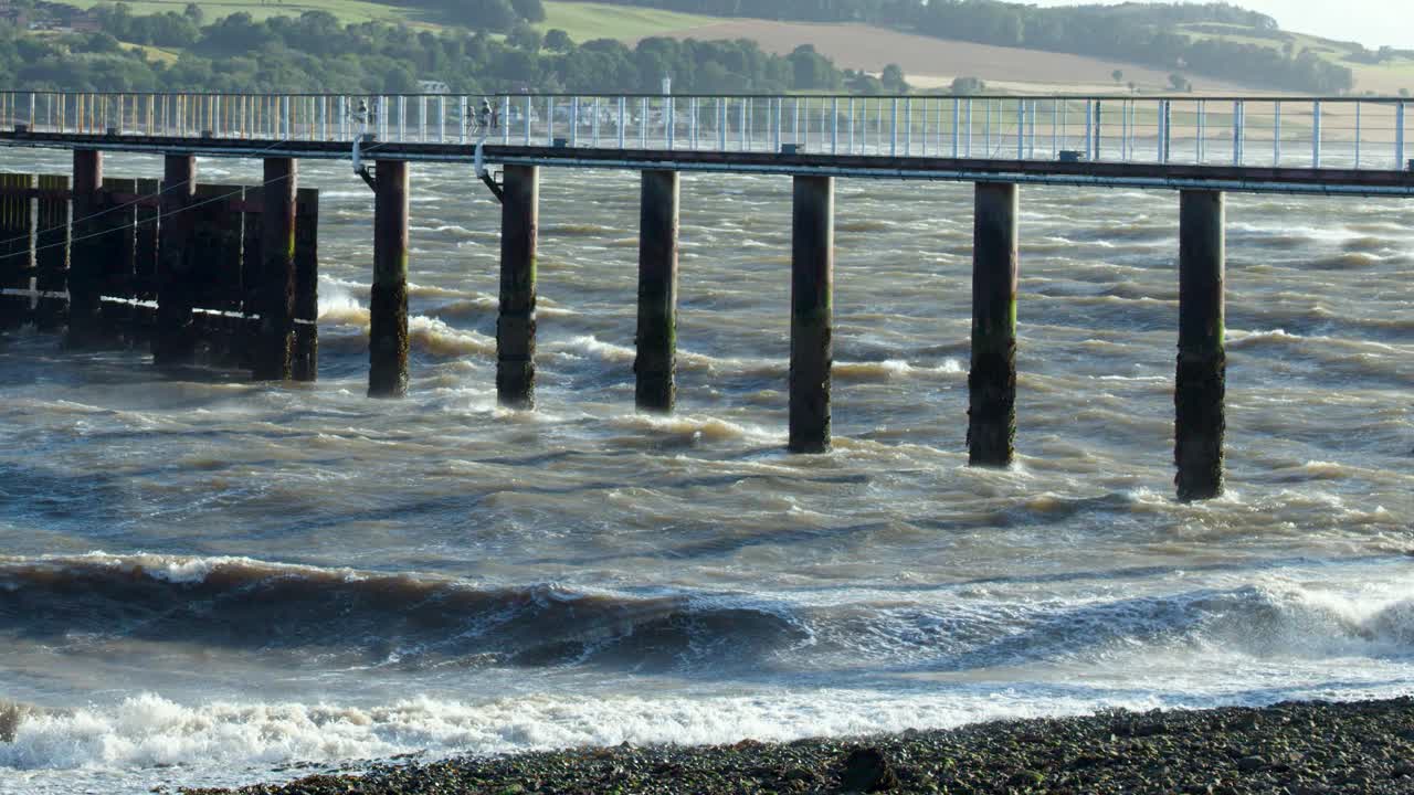 Strong sea waves hit a pier structure on a rocky beach in Broughty Ferry, Scotland