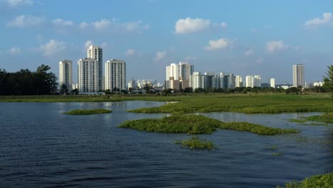 aerial drone dolly-in and rising shot of the south part of são paulo, brazil from the man-made guarapiranga reservoir towards the socorro neighborhood with skyscrapers and houses on a fall evening