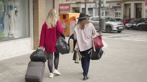 two women walking with luggage on a city street