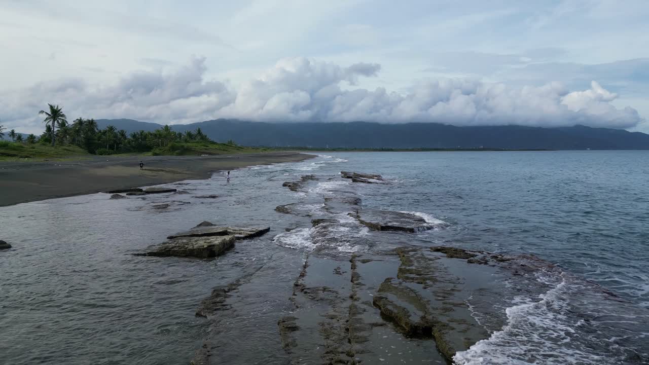 toma aérea de drones de olas rompiendo en rocas costeras mientras la niña camina en la playa