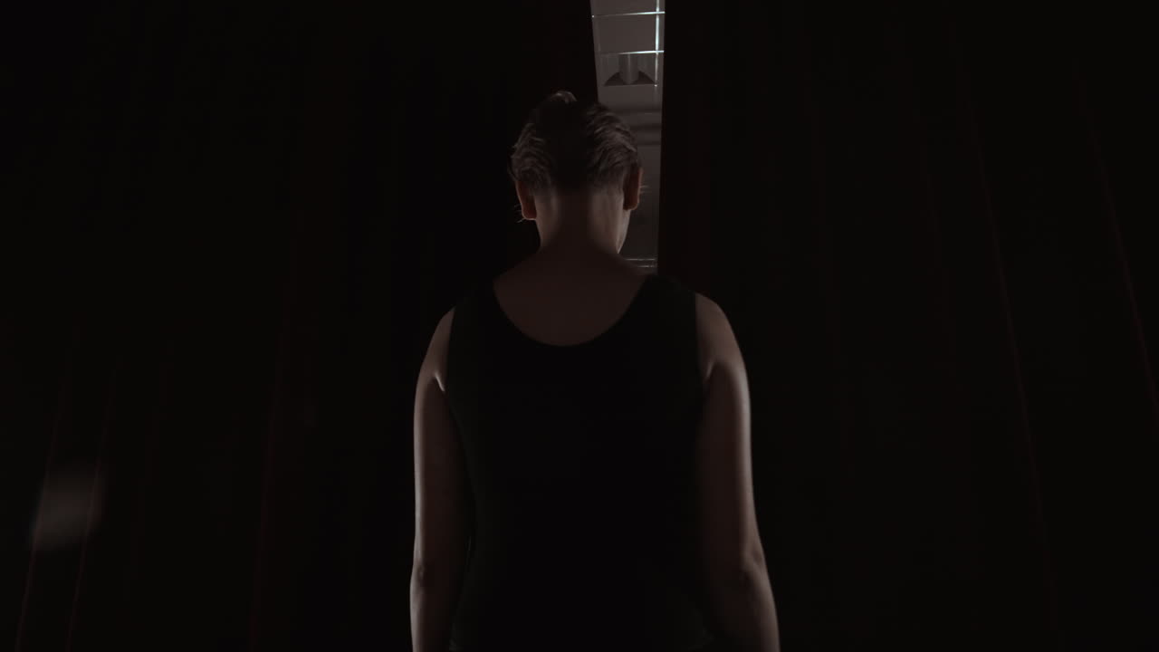 젊은 프리마 발레리나가 무대에 들어오고 관객 앞에 커튼이 열리면서 어두운 무대 희생 유연성 연기 실루 느린 동작