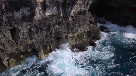 aerial close up view of waves crashing on an eroded and rugged sea cliff