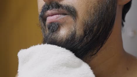 a closeup footage of a young man drying his beard with a white towel, with blurred background. hygiene concept