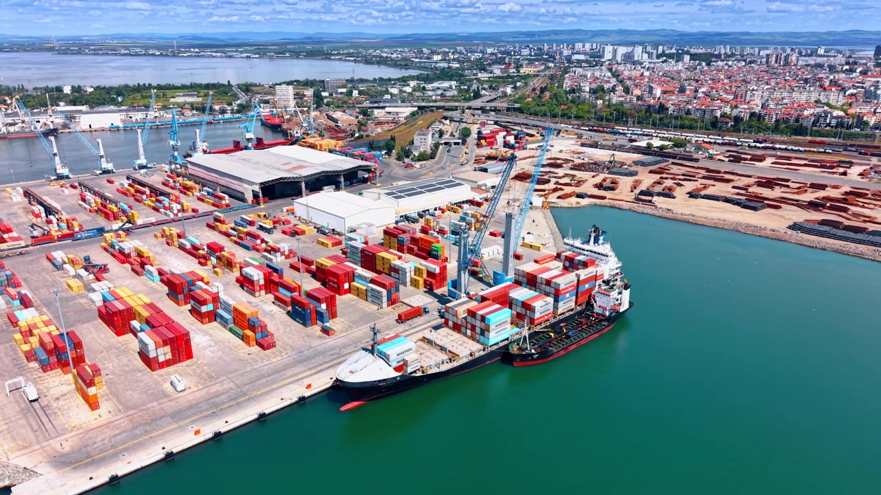 Burgas, Bulgaria, 21 May 2026: Elevated view of container port operations at Burgas, Bulgaria. Cargo ship at berth with crane loading, colorful containers on terminal and city panorama.